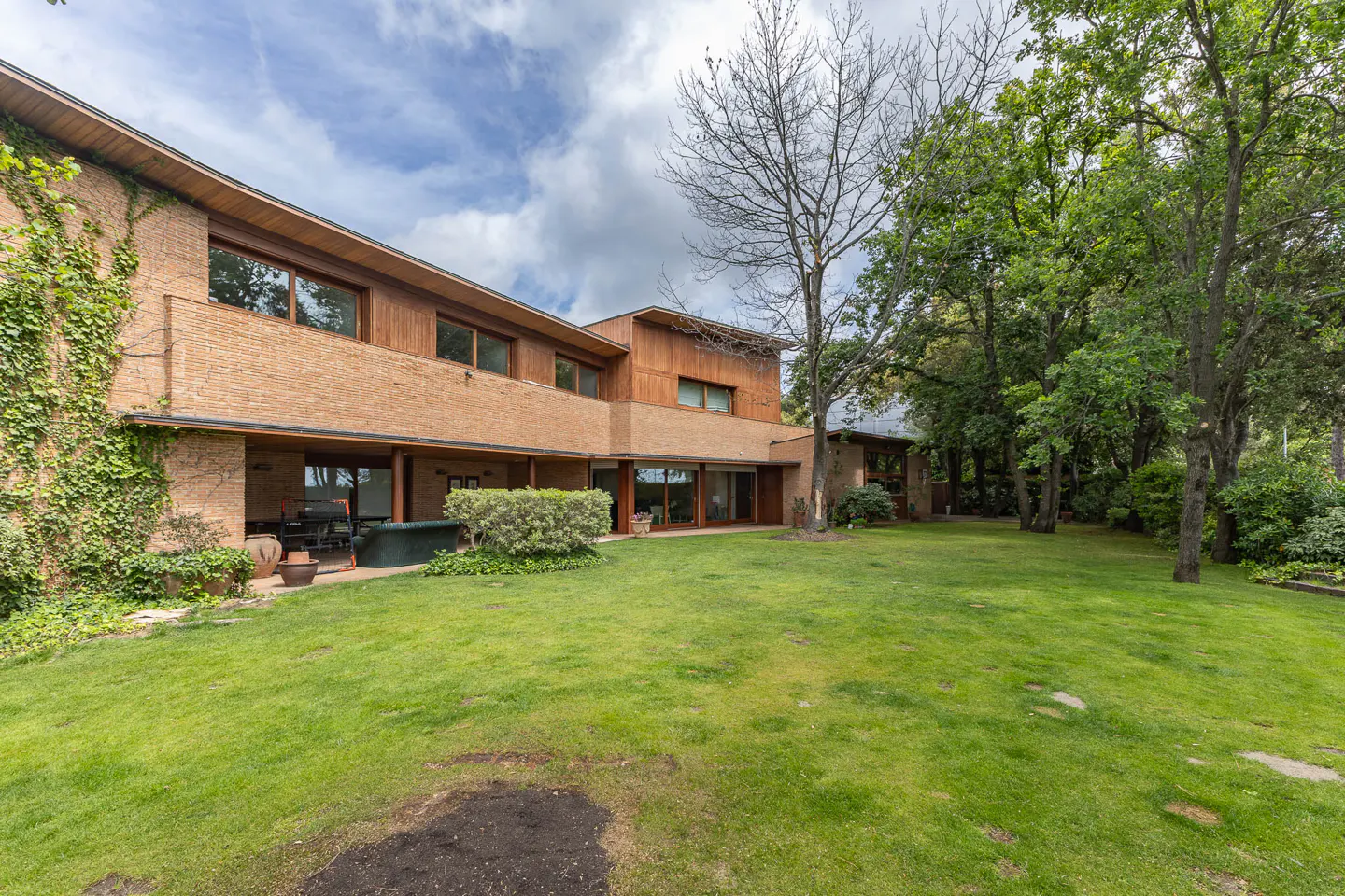 Exterior view of a two-story brick and wood home with a large green lawn and trees.