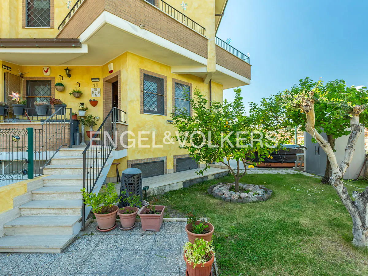 Exterior view of a two-story yellow house with a garden, stairs, and the Engel & Völkers logo.