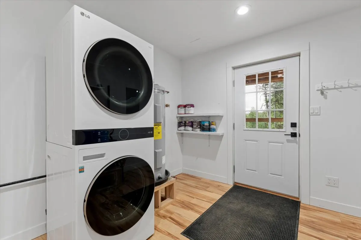 Bright laundry room with stacked white LG washer/dryer, water heater, and white door with window to the outside.