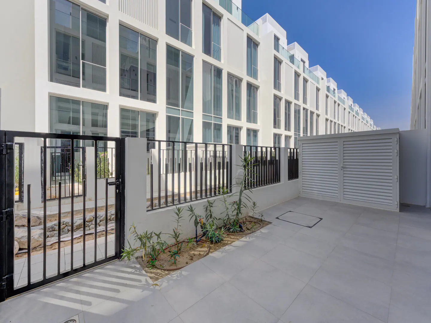 Exterior view of a modern white building with large windows, a black metal gate, and a white storage unit.