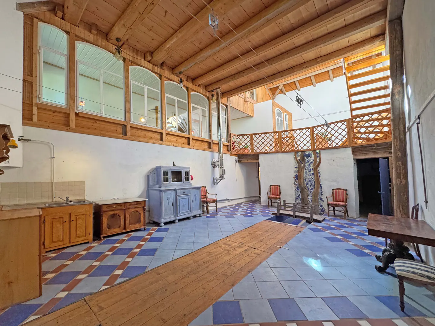 Interior view of a large room with a wooden ceiling, blue and white tiled floor, and antique furniture.