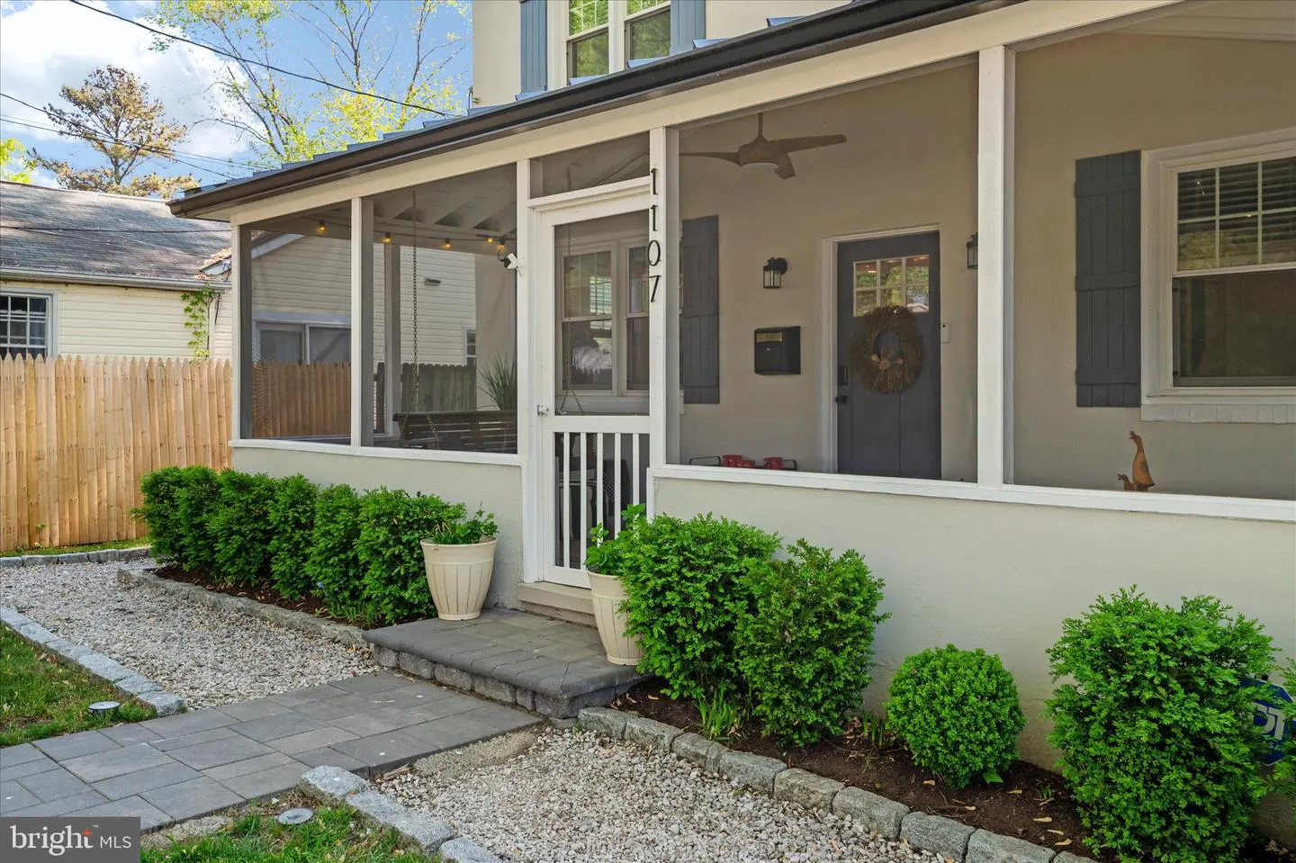 Exterior view of a house with a screened-in porch, gray door with wreath, and manicured landscaping.