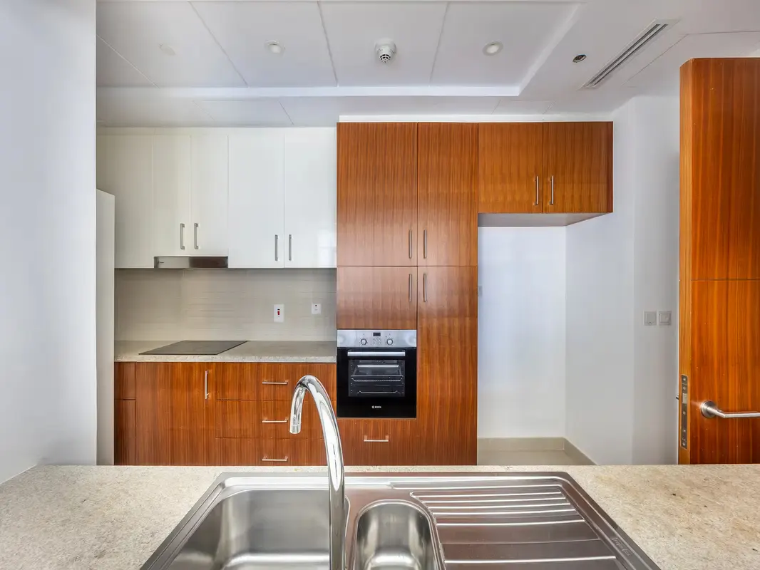 A modern kitchen with white and wood cabinets, stainless steel sink, and built-in oven.