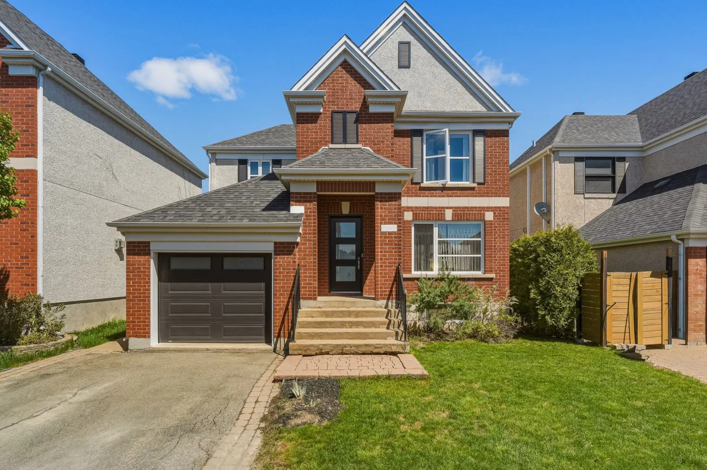 Two-story red brick house with a gray roof, black front door, and a garage on a sunny day.