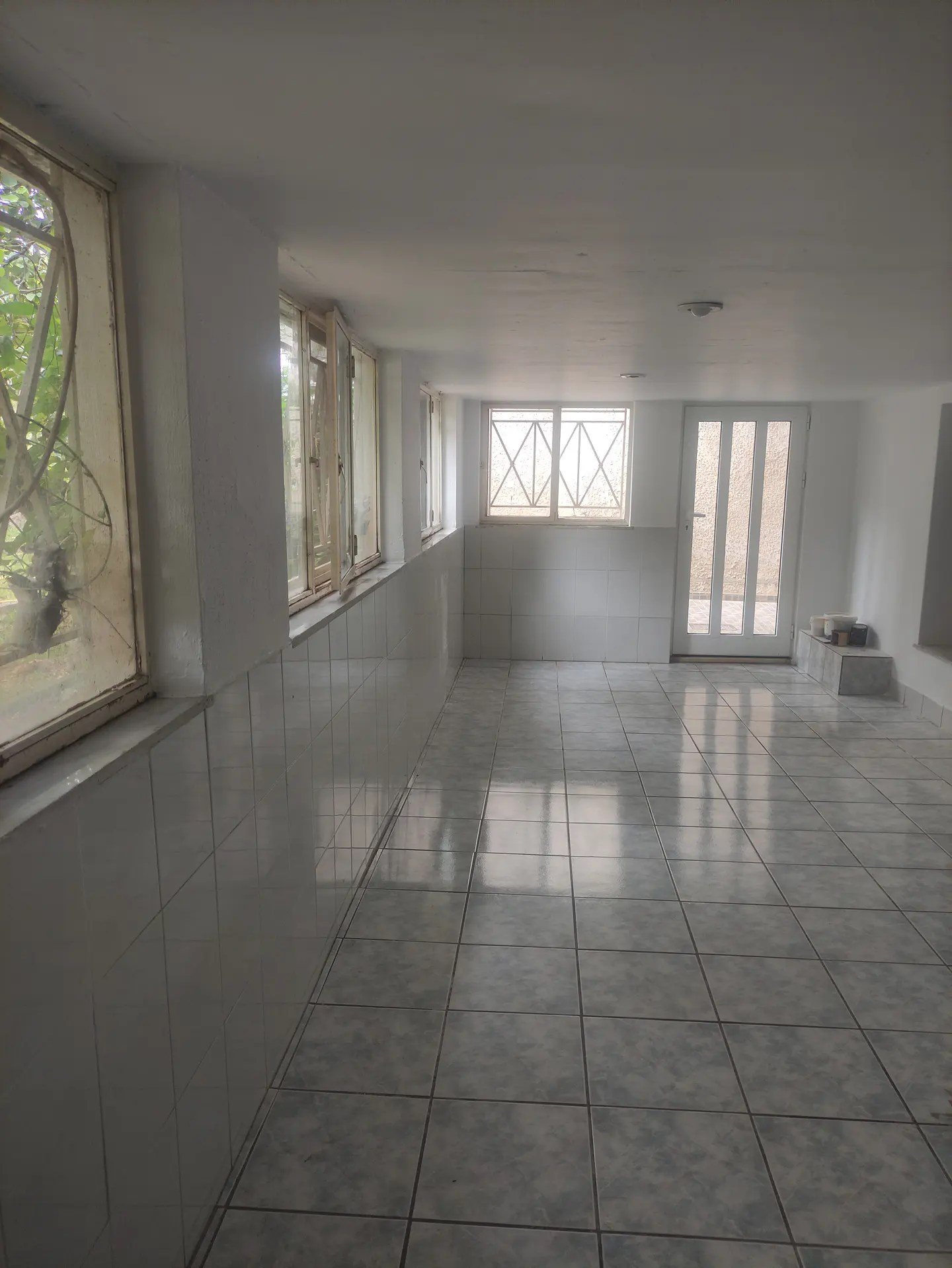 A bright, empty basement room with tiled floors and walls, and several windows.