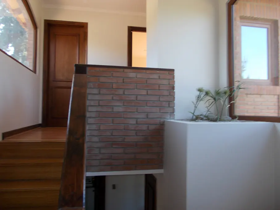 Interior view of a home featuring a wooden staircase, brick wall, and a planter with greenery near a window.