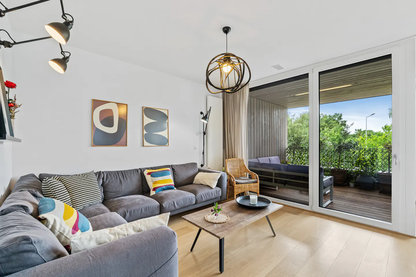Modern living room with a grey sectional sofa, wooden coffee table, and large sliding doors opening to a balcony.