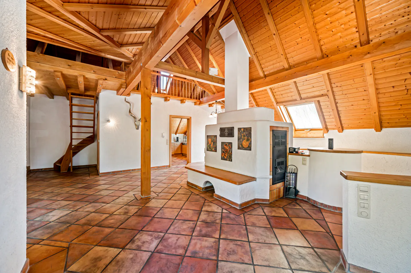 Attic living space with exposed wood beams, terracotta tile floor, and a white fireplace with artwork. A wooden ladder leads to a loft area.