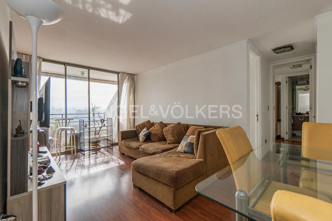 Bright living room with brown sectional sofa, glass table, and balcony with city views.