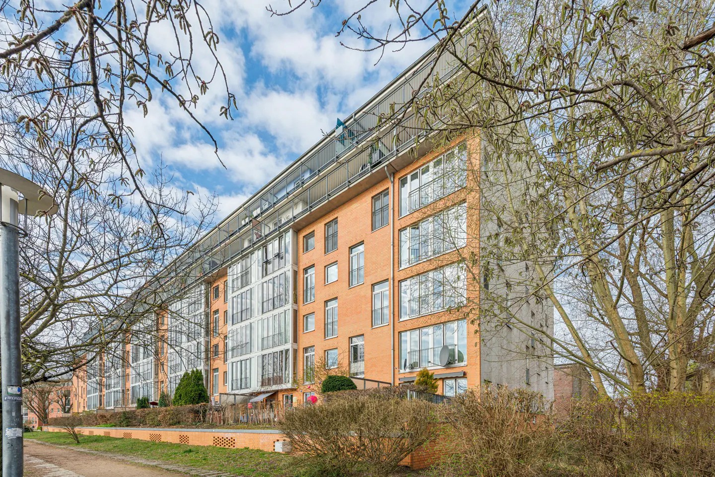 Exterior view of a modern orange brick apartment building with balconies and large windows on a partly cloudy day.