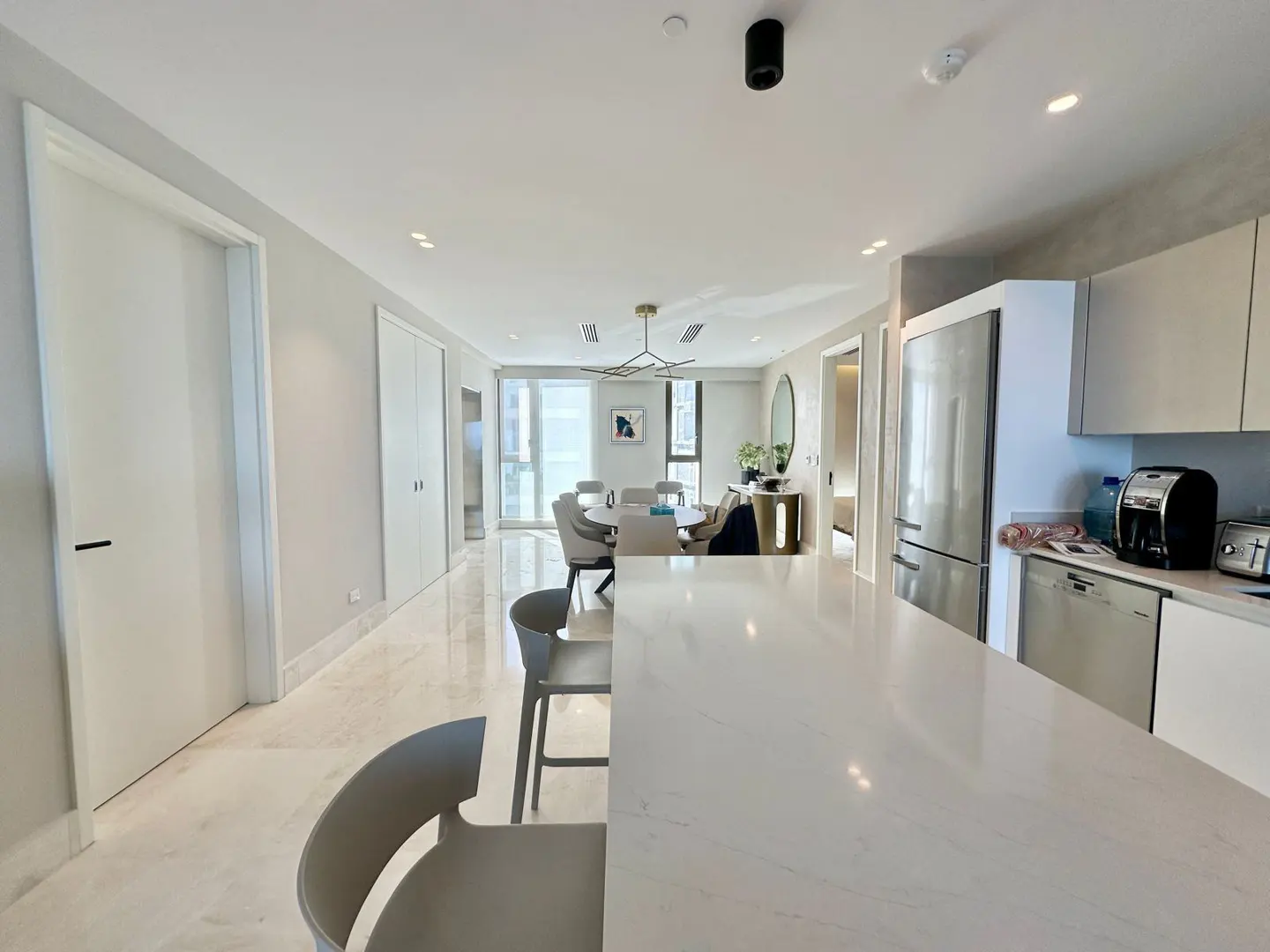 A bright, modern apartment interior with a kitchen island, dining area, and marble floors.