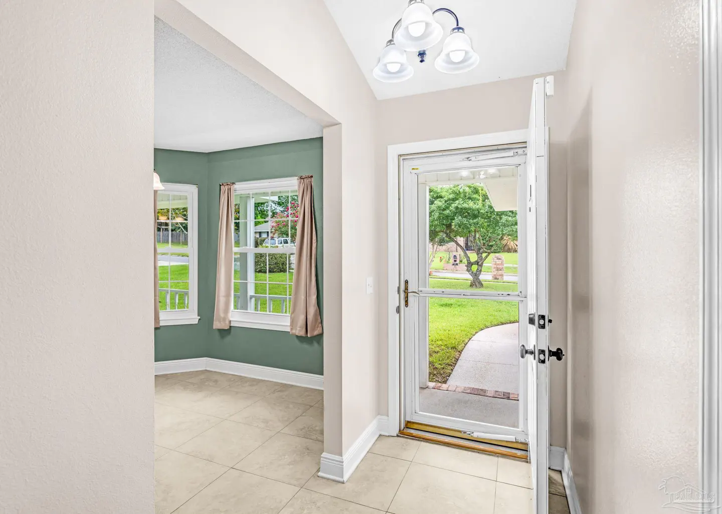 Foyer with beige tile floor, open white door to yard, and green dining room with two windows.