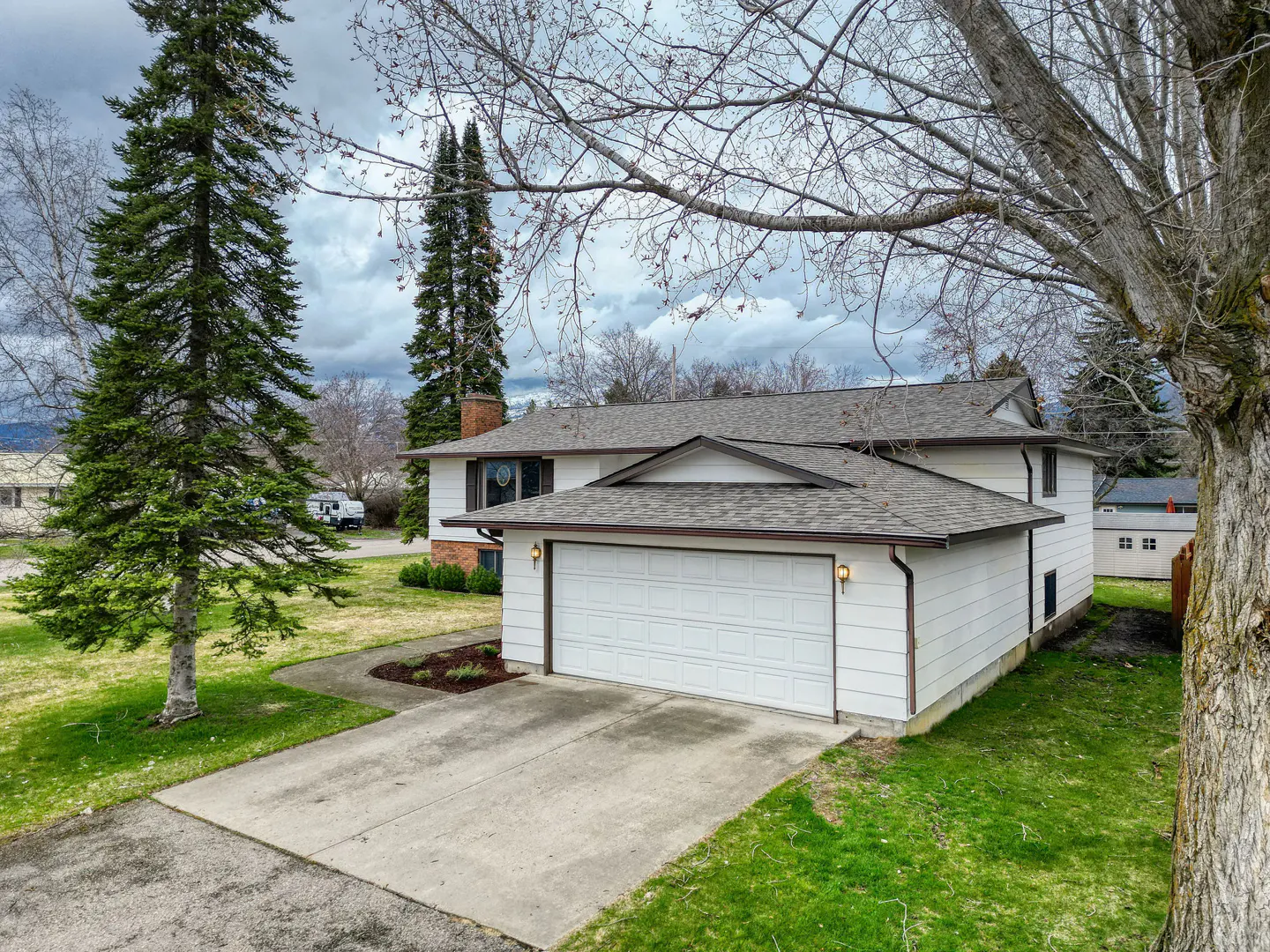 Two-story white house with a gray roof and a two-car garage, surrounded by green grass and trees.