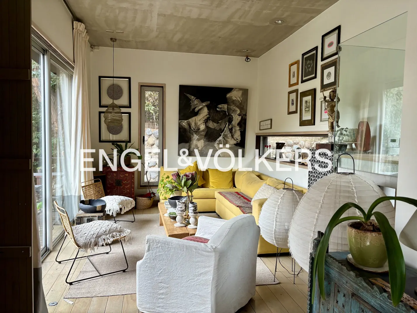 Cozy living room with a yellow sectional sofa, white armchair, wooden coffee table, and gallery wall art on white walls.
