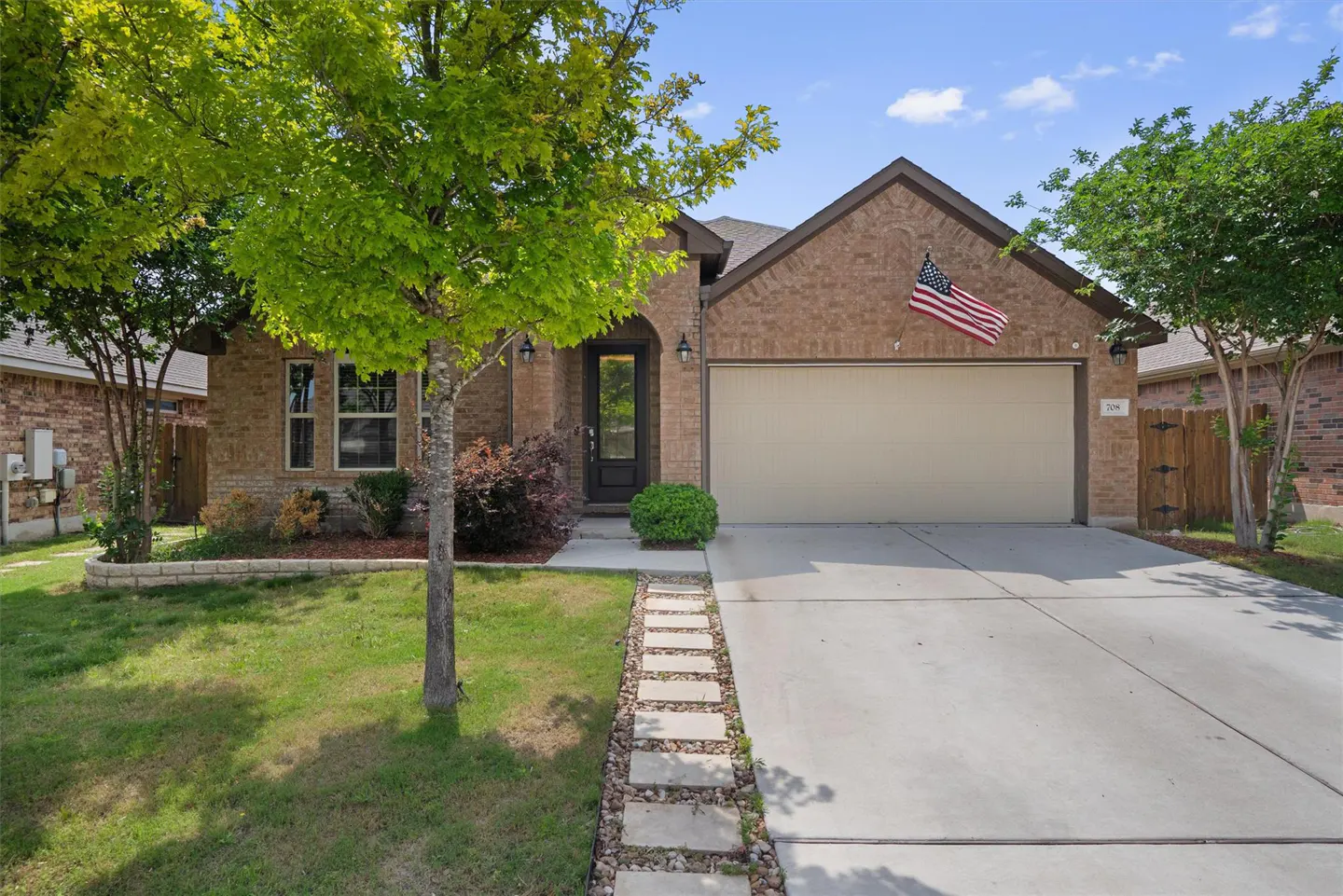 A single-story brick house with a two-car garage, a green lawn, and an American flag.
