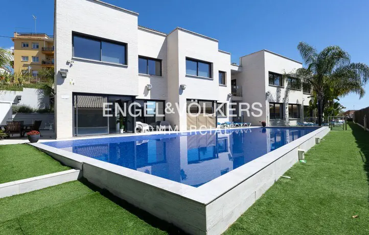 Modern white house with a blue pool, green lawn, and palm trees under a clear blue sky.