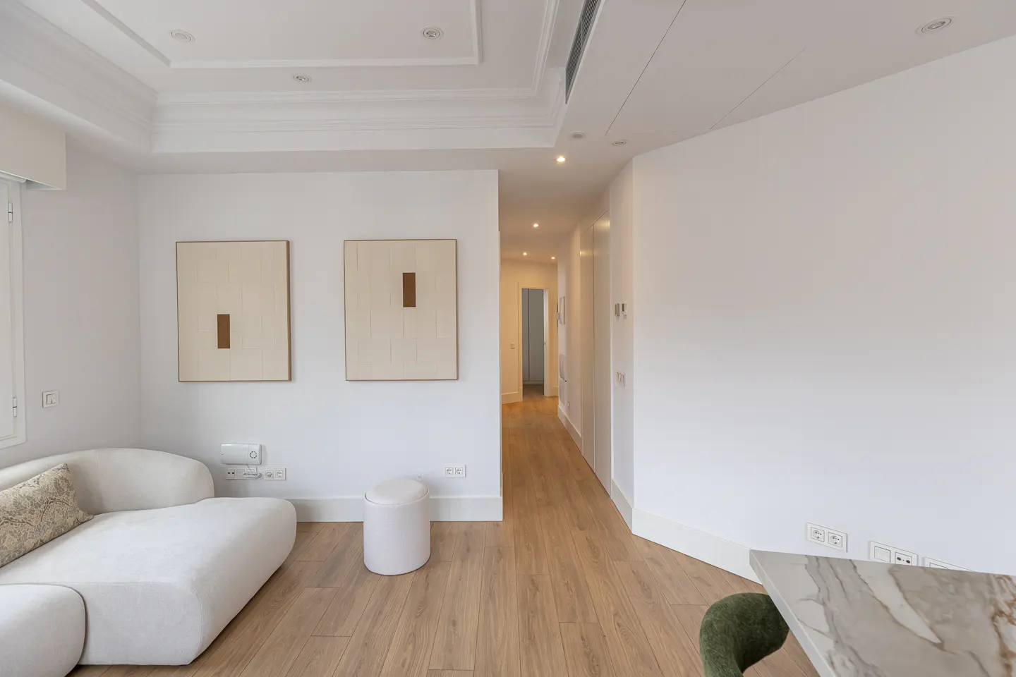 Bright, modern living room with white walls, light wood floors, and minimalist decor. A white sofa and artwork add to the clean aesthetic.