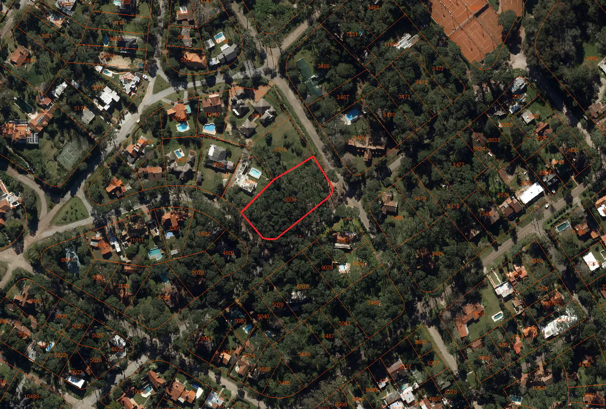 Aerial view of a wooded residential area with a vacant lot outlined in red. Houses and streets are visible.