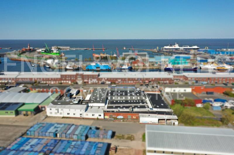 Aerial view of a harbor with industrial buildings, shipping containers, and various boats docked in the blue water. [AI-generated text]