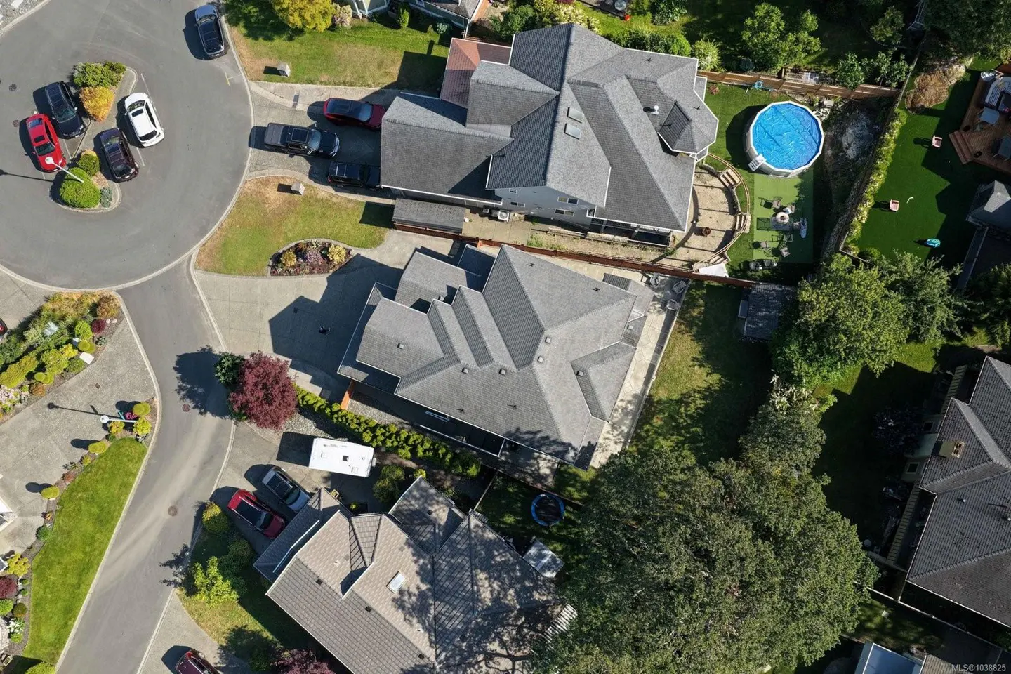 Aerial view of suburban homes with grey roofs, a circular cul-de-sac, and a backyard with a round blue swimming pool.