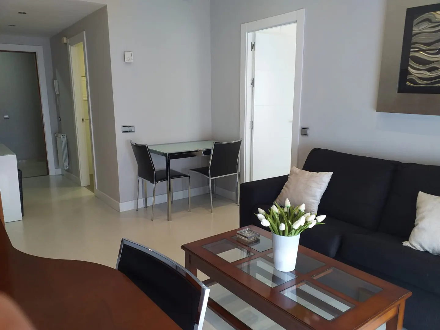 Living room with black sofa, wood coffee table with tulips, and dining table with black chairs. Gray walls and white doors.