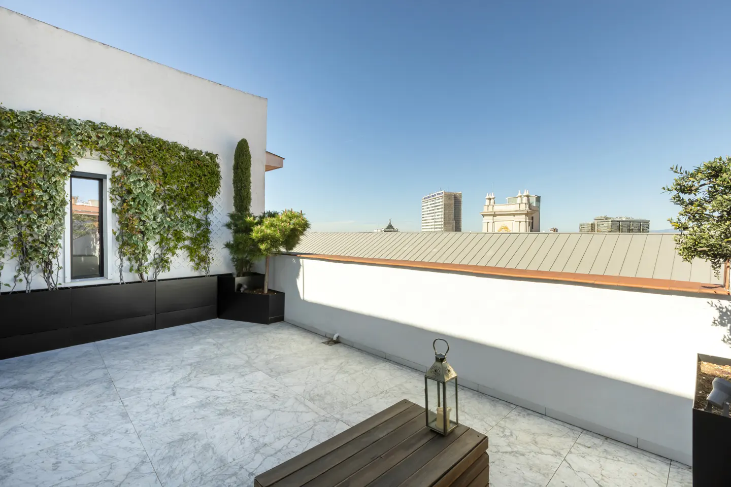 Rooftop terrace with marble flooring, a vertical garden wall, a wooden table with a lantern, and city skyline views.