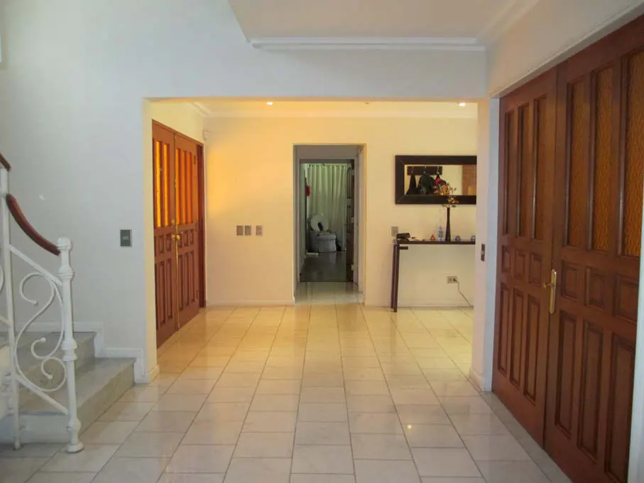 A bright foyer with white walls and tiled floors. A staircase is on the left, and a bathroom is visible through an archway.