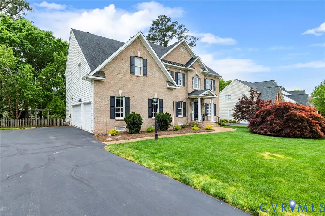 Two-story brick house with black shutters, a black roof, and a green lawn under a blue sky.