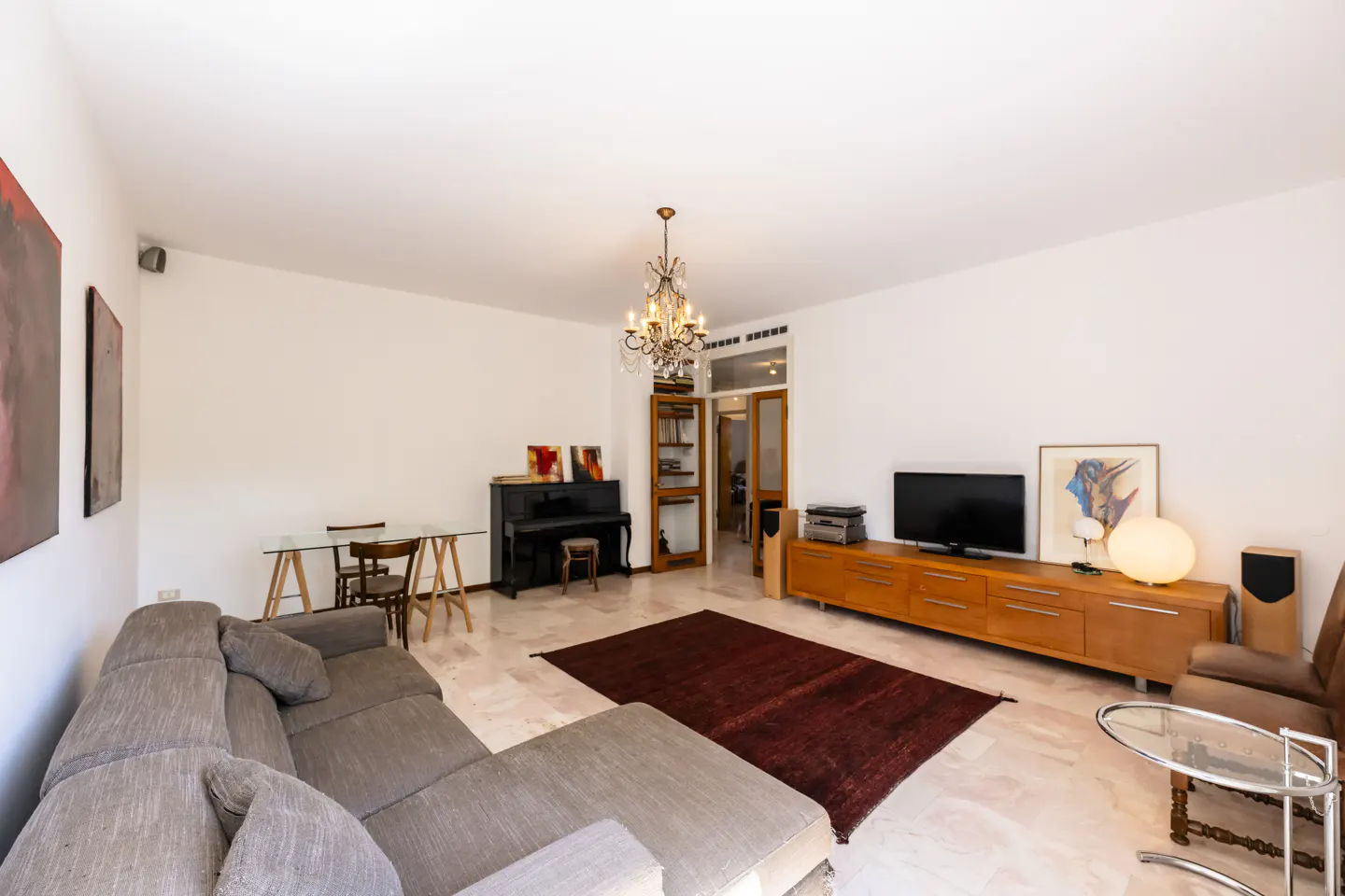 Bright living room with a gray sectional sofa, a black piano, a TV, and a chandelier.