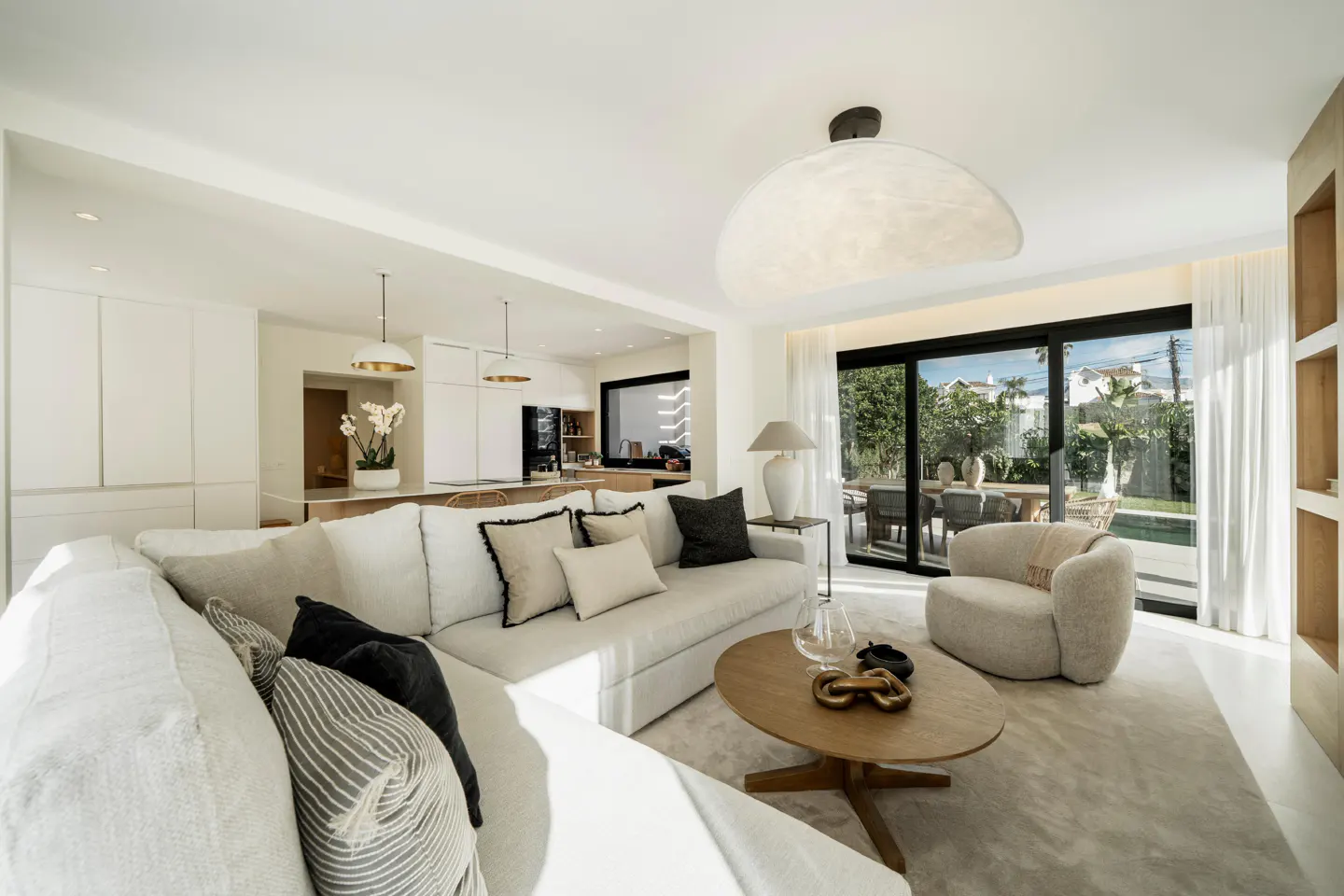 Modern living room with a white sectional sofa, round wooden coffee table, and a view of a patio through sliding doors.