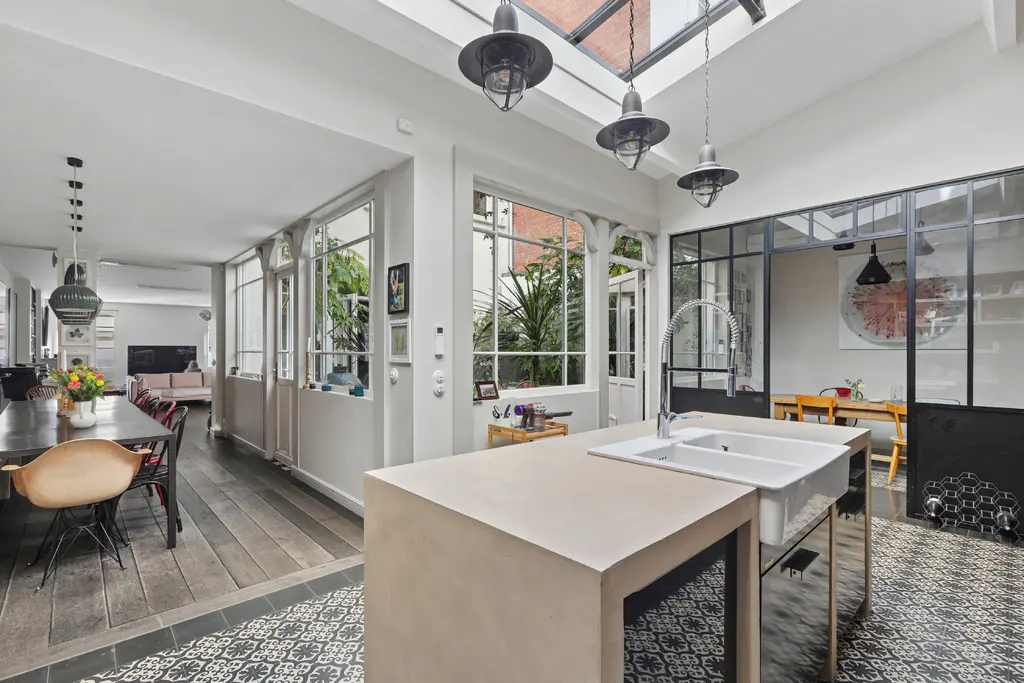 Bright, open kitchen with skylights, island with white sink, and black-framed glass doors. Dining table and chairs visible in the background.