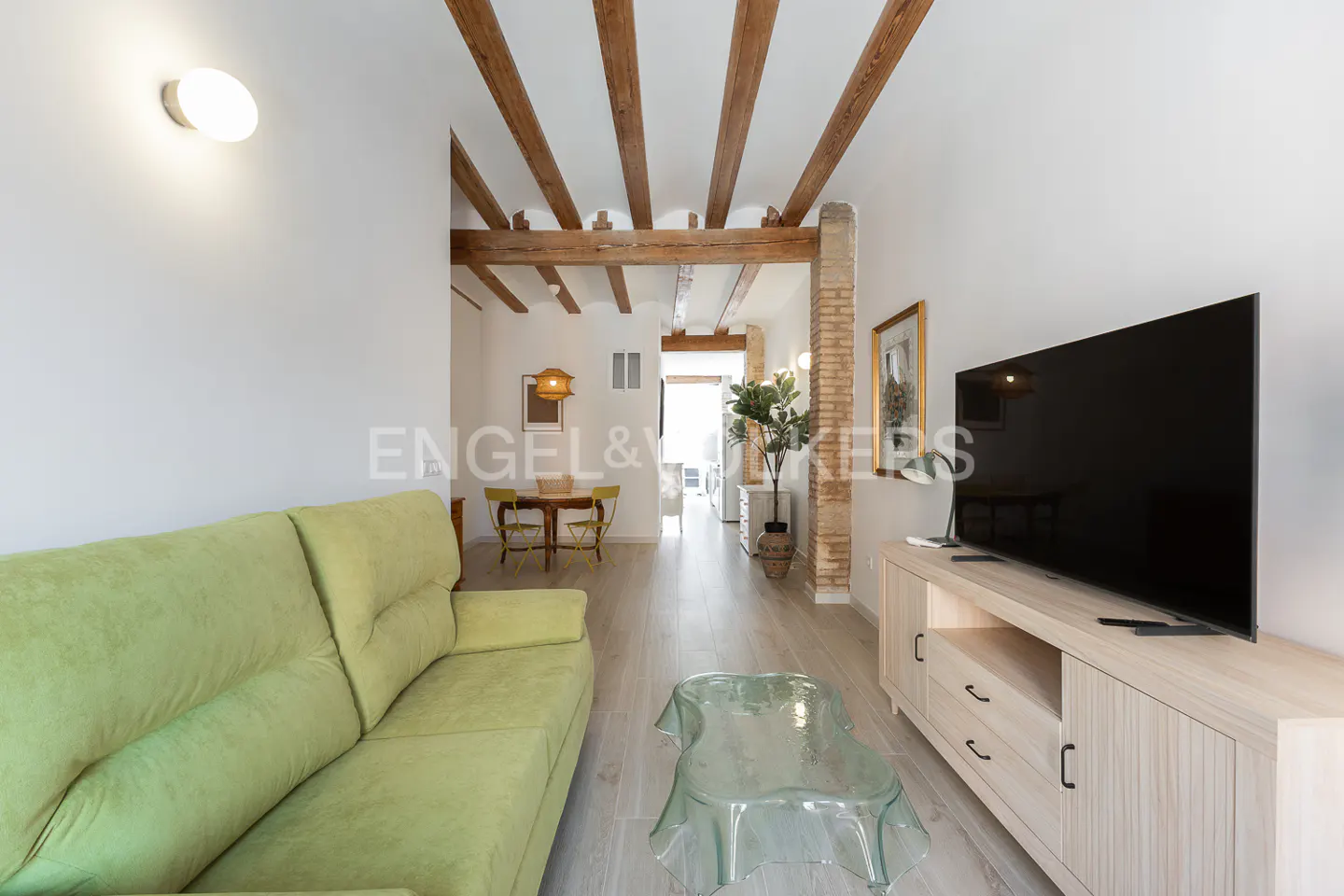Living room with a green sofa, clear coffee table, TV, and wooden beams on the ceiling.