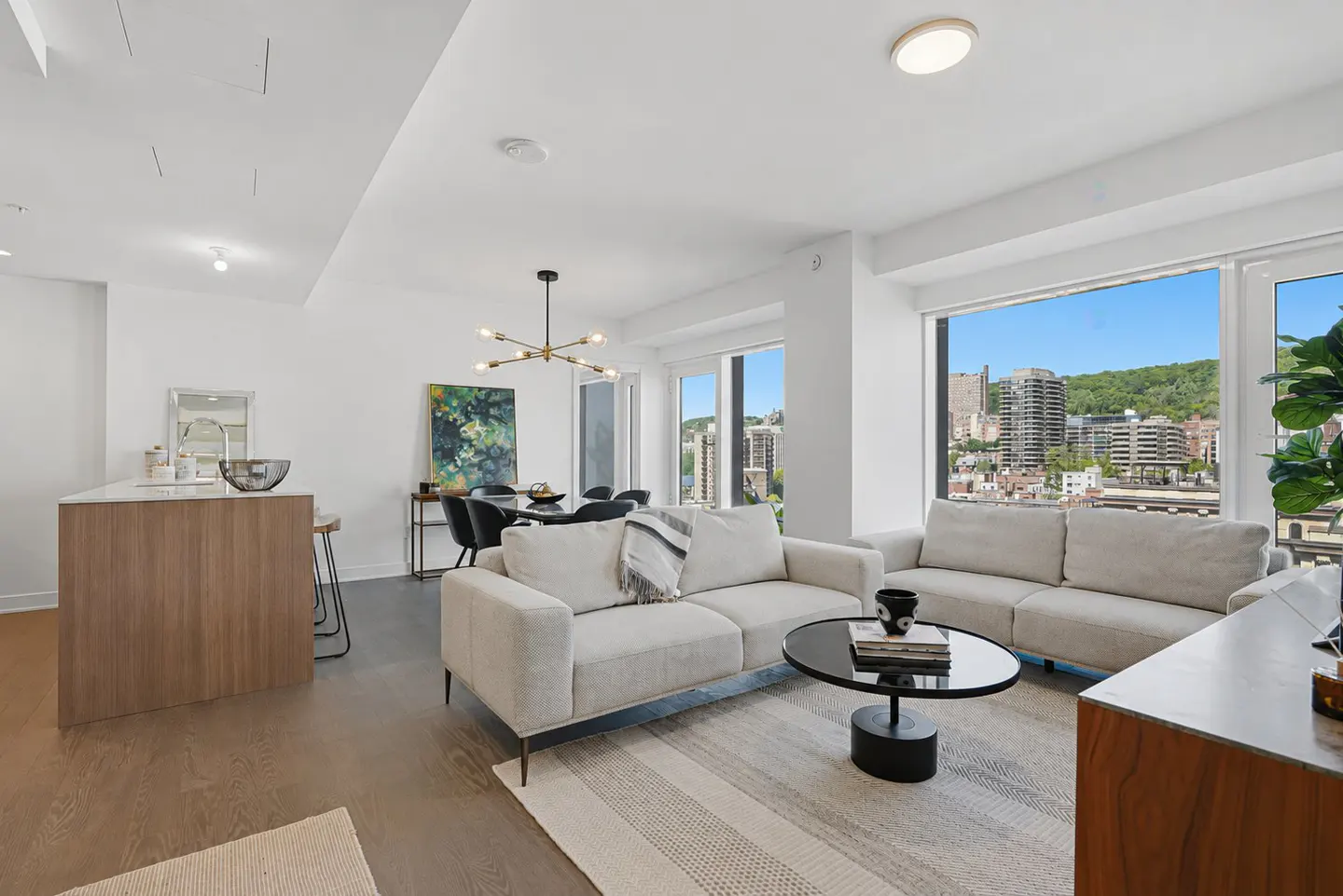 Modern open-concept living room with white sofas, a round coffee table, and large windows overlooking a city skyline.