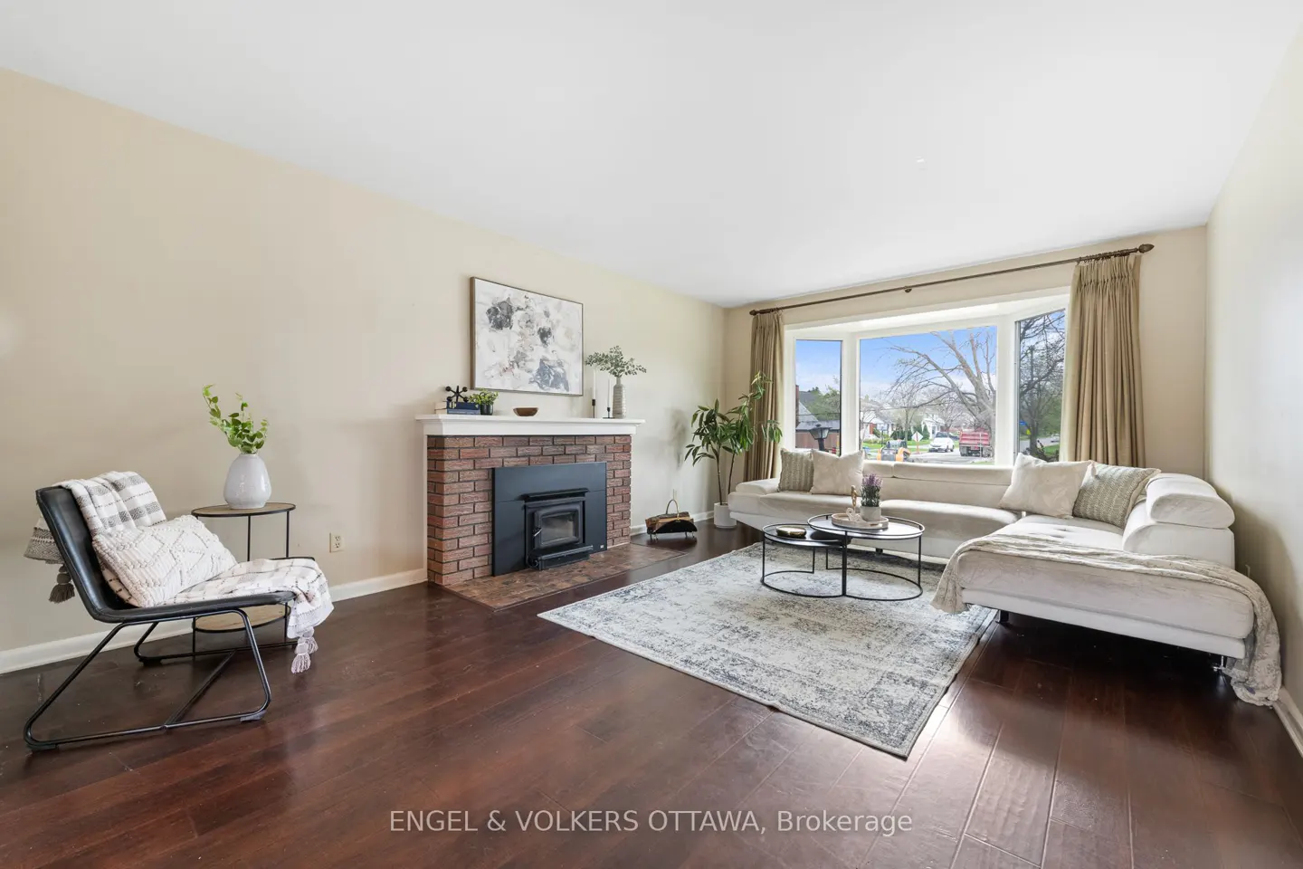 Living room with dark wood floors, a brick fireplace, and a large window with a beige sectional sofa.