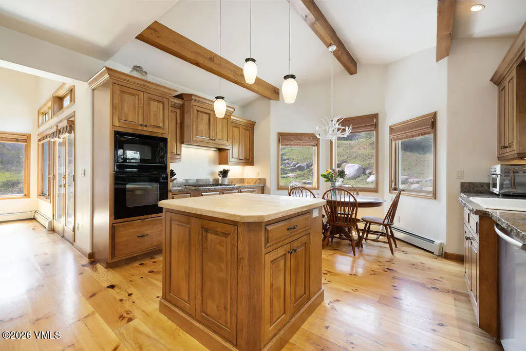 A bright kitchen with wood cabinets, island, and floors. A dining table sits near windows with a view.