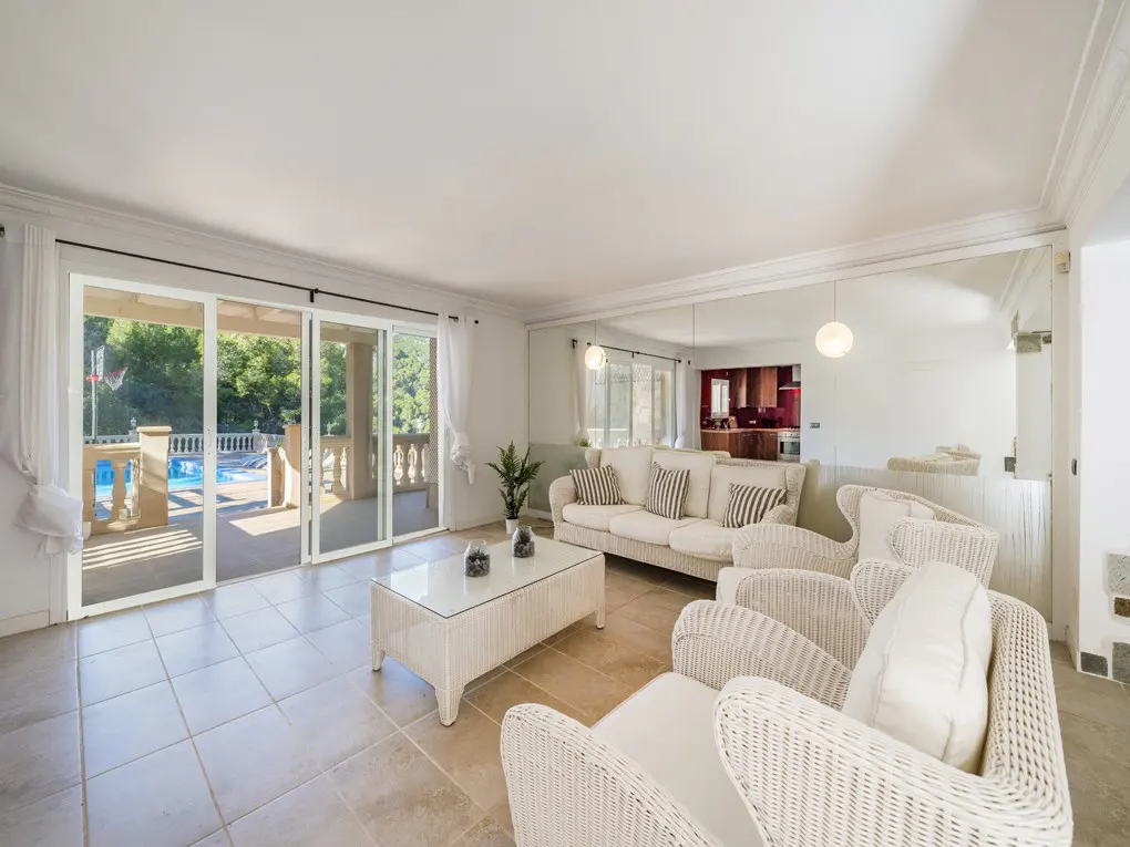 Bright living room with white wicker furniture, a glass coffee table, and sliding doors to a balcony overlooking a pool.