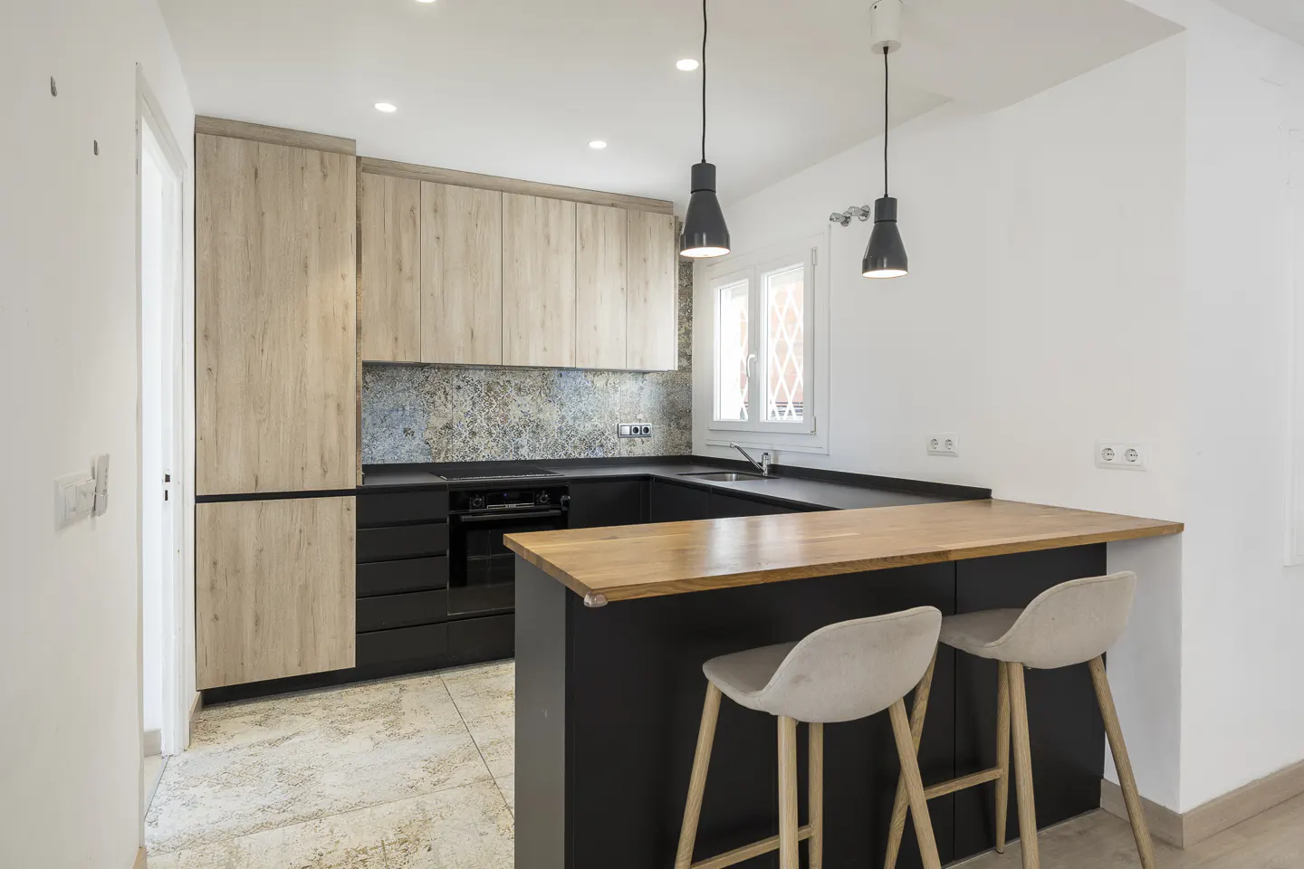 Bright kitchen with wood cabinets, black countertops, and a breakfast bar with two stools. Two pendant lights hang above the bar.