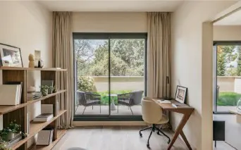 A bright home office with a desk, chair, and bookshelf. Sliding glass doors open to a patio with chairs and greenery.