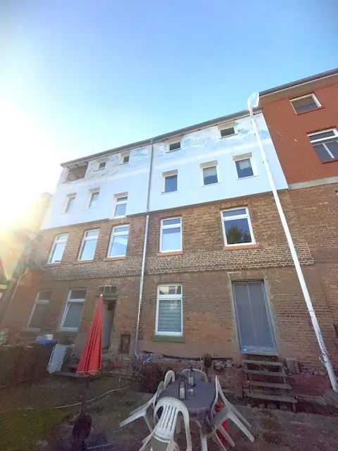 Exterior view of a brick building with white trim and windows, a backyard with a table, chairs, and a red umbrella.