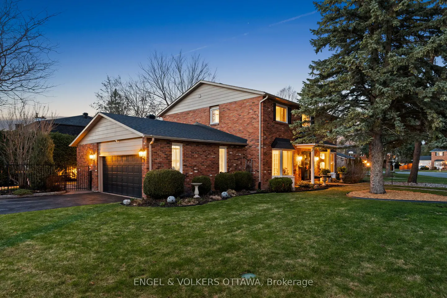 Exterior view of a two-story red brick house with a green lawn and a dark blue sky at dusk.