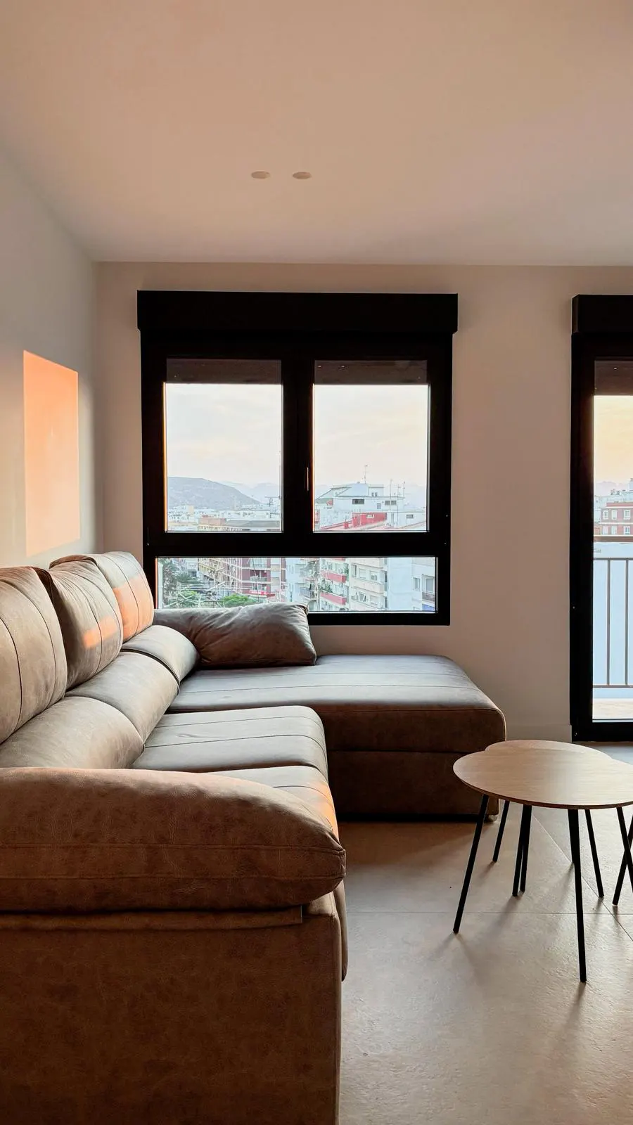 Modern living room with a brown sectional sofa, round coffee table, and large windows with a city view.