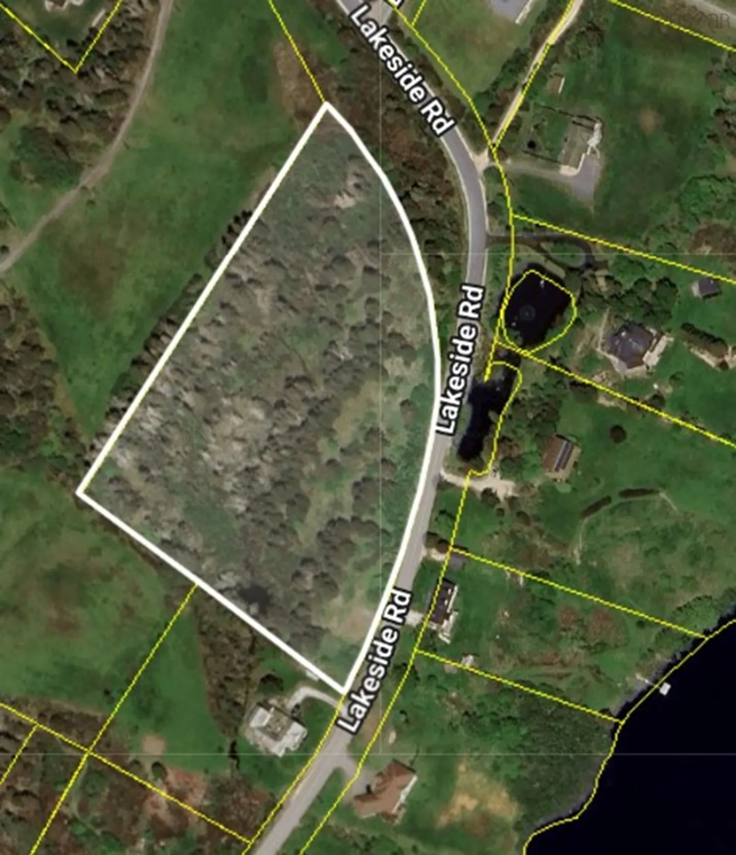 Aerial view of a wooded lot outlined in white, adjacent to Lakeside Rd, with green grass and scattered houses nearby.