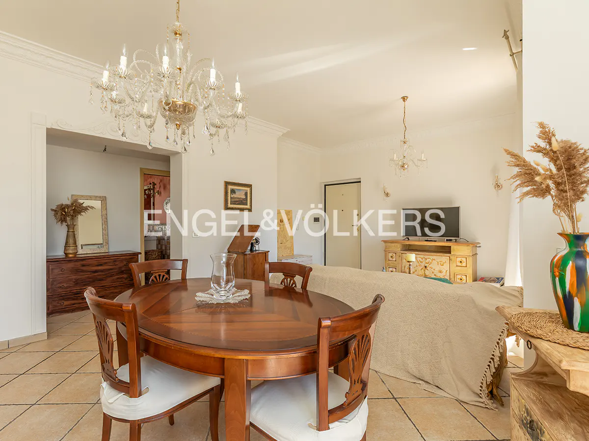 Interior view of a dining room with a wooden table and chairs, a chandelier, and a view into a living room.
