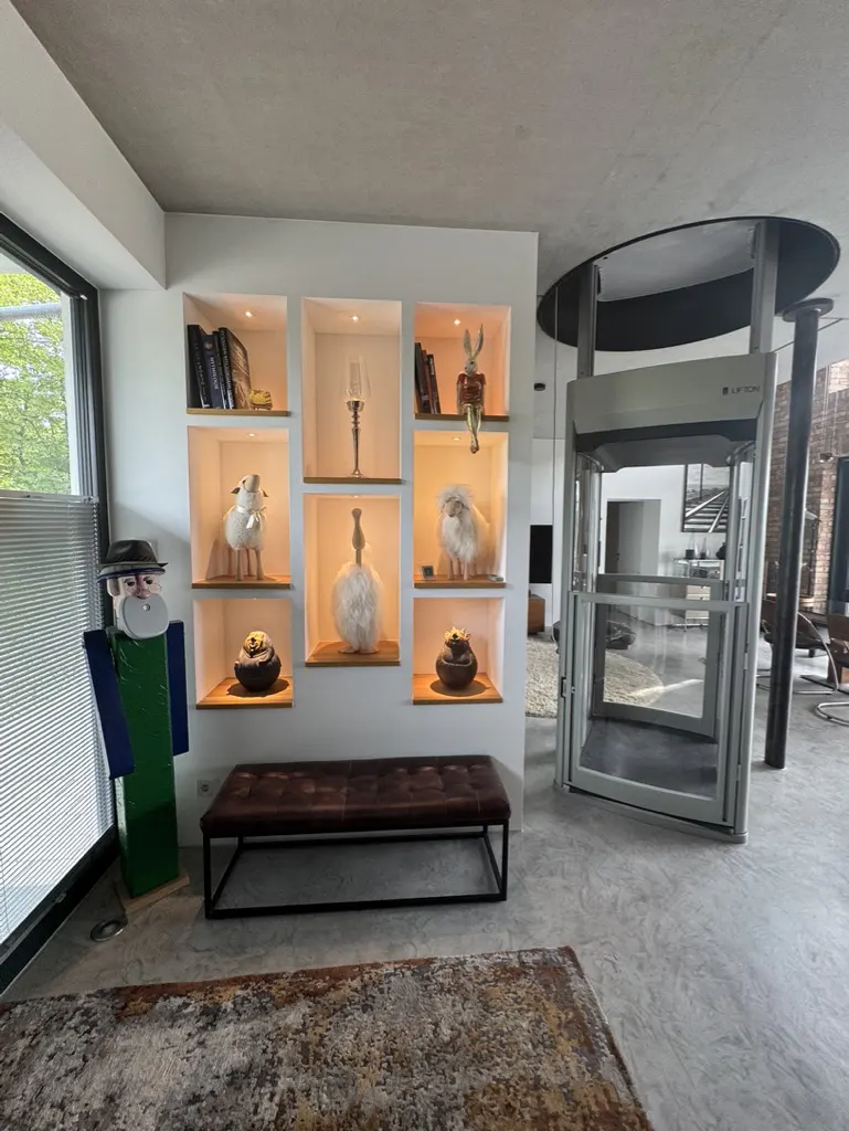 Modern interior with a lit wall niche display, a leather bench, a decorative figure, and a glass residential elevator.