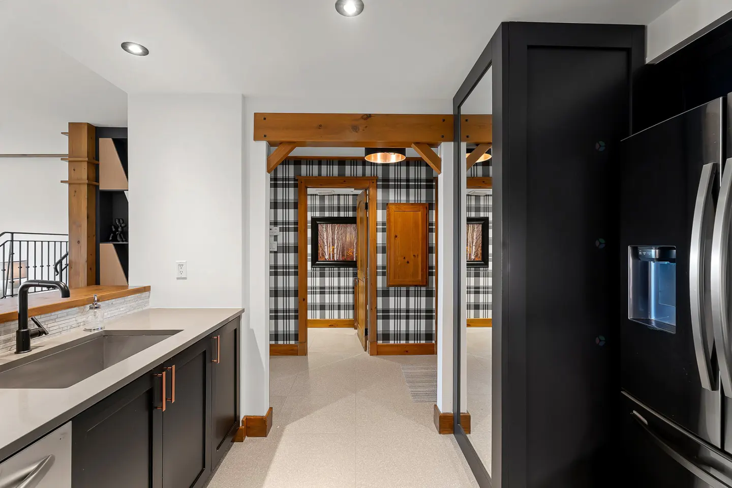 Interior view of a modern kitchen with black cabinets, stainless steel appliances, and a hallway with plaid wallpaper.