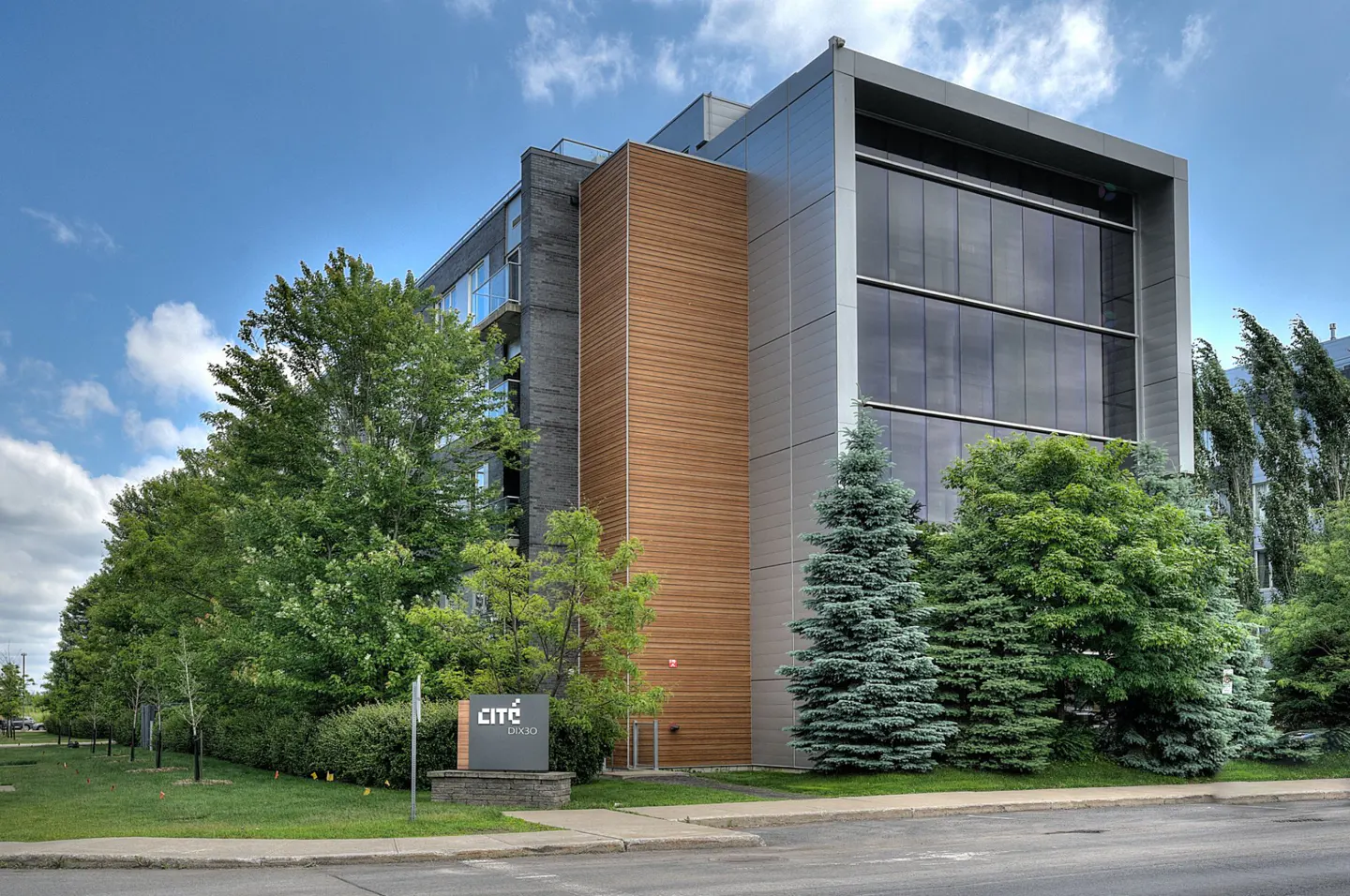 Exterior view of the Cite Studio building with a modern design, featuring wood and metal accents, surrounded by green trees.