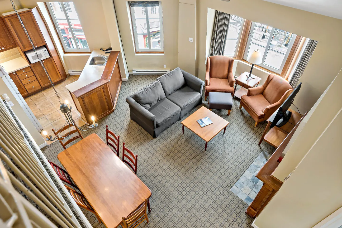 Overhead shot of a living room with a gray sofa, two brown armchairs, a wooden table, and a dining table with chairs.