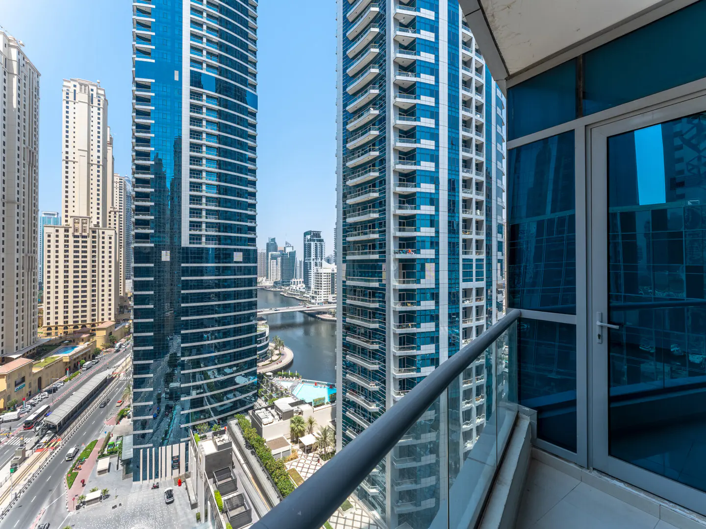 View from a balcony with a glass railing, overlooking blue glass skyscrapers and a river in a city.