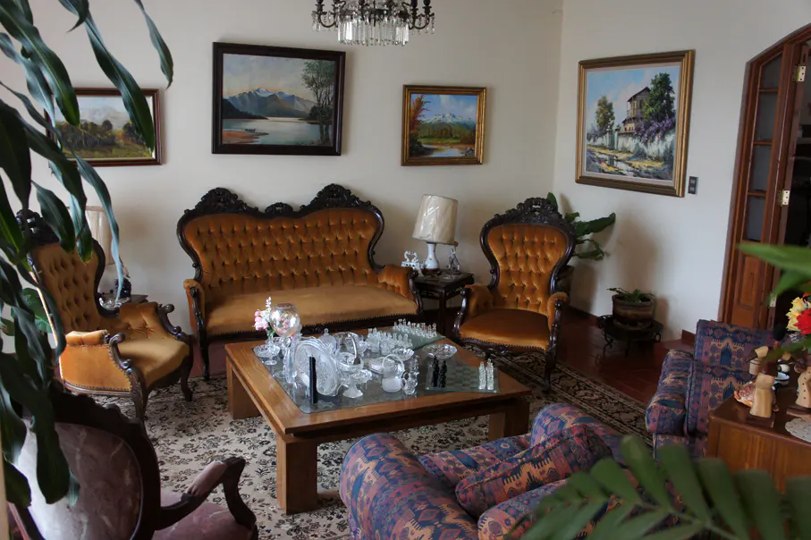 Ornate living room with brown velvet sofas, landscape paintings, and a glass-topped coffee table with crystal decor.