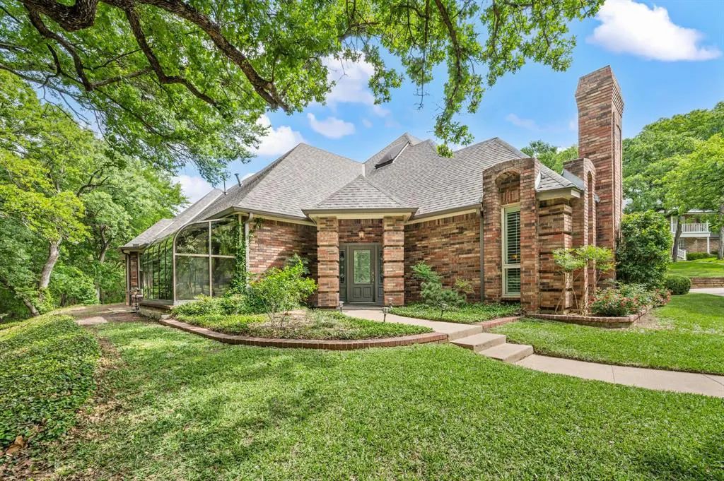 Brick house with a gray roof, green lawn, and a tall brick chimney under a blue sky with trees.